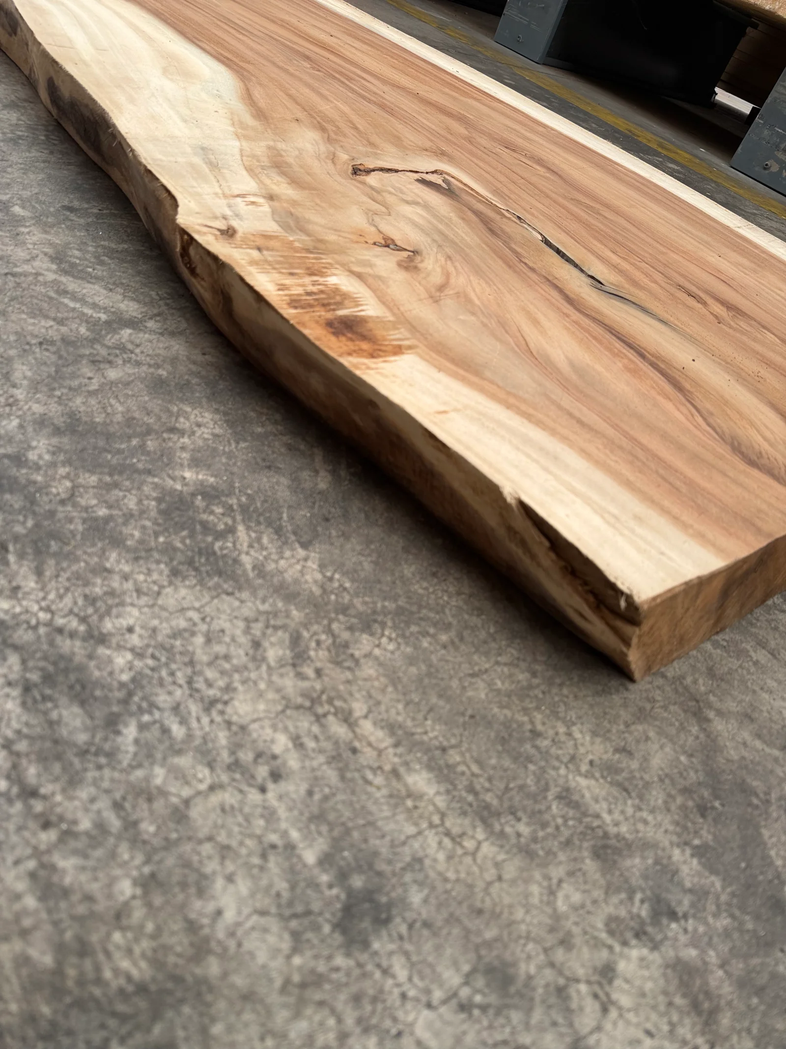 Low-angle edge view of the Saman slab showing thickness and live-edge profile, with pale sapwood beside warm brown grain; captured thickness 90 mm.